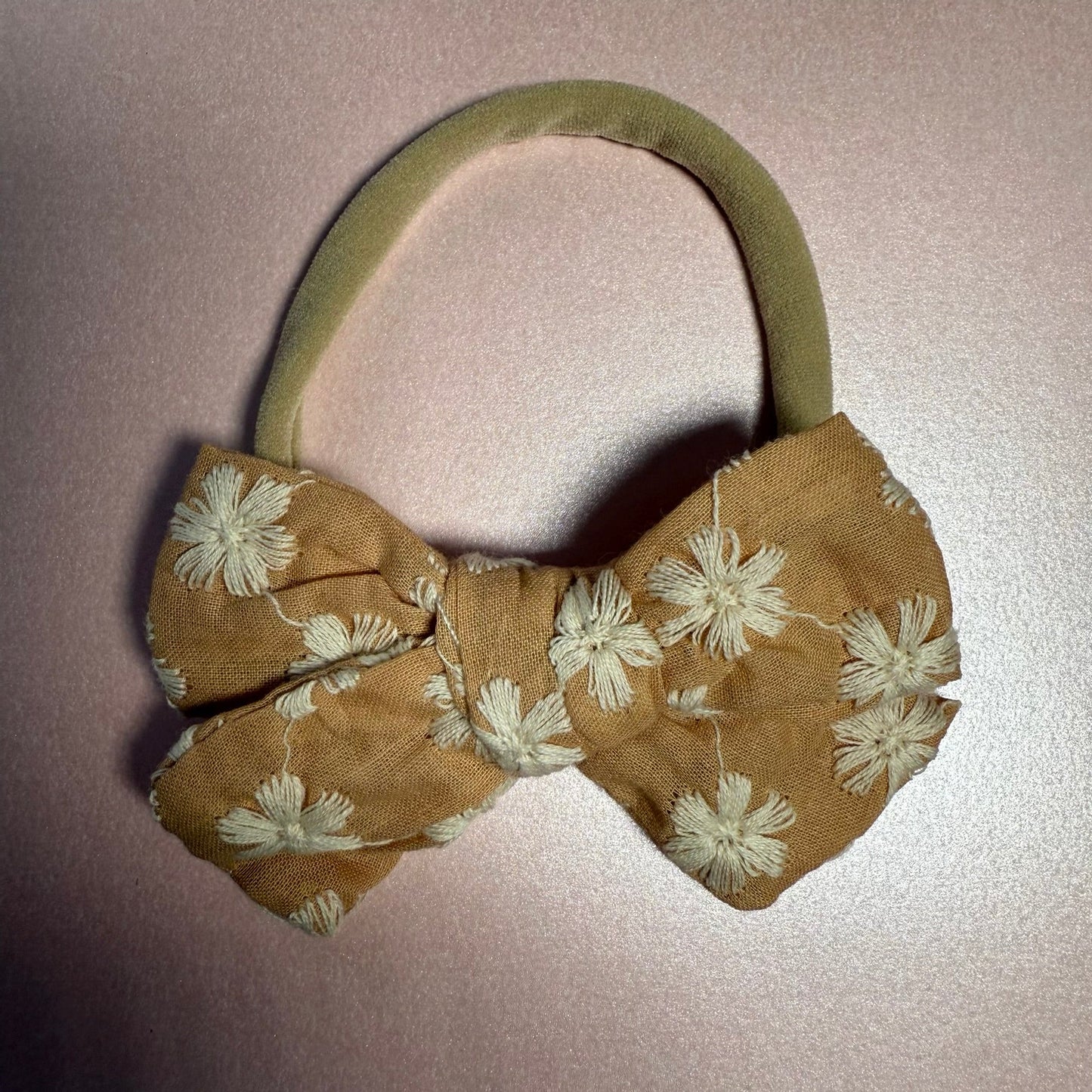Brown floral bow headband on a light pink background