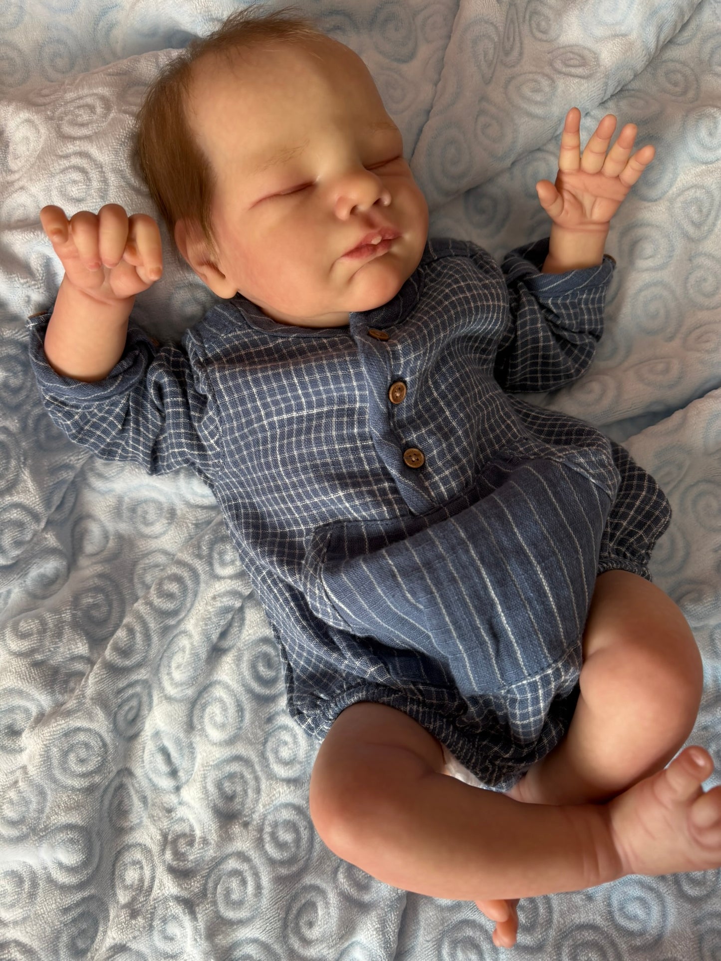 Newborn baby wearing a checkered outfit lying on a patterned blanket