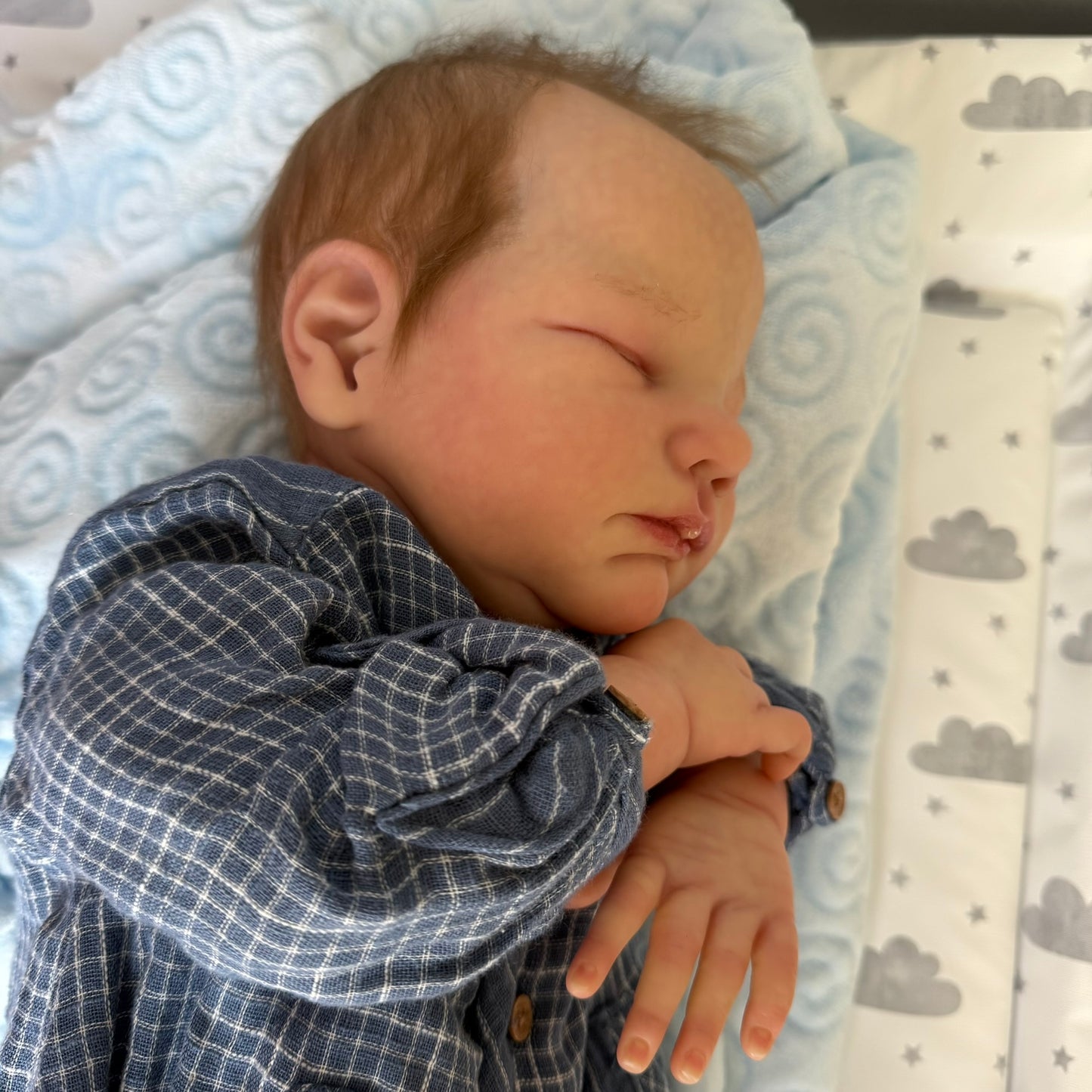 Newborn baby sleeping on a blue checkered blanket with a cloud-patterned blanket in the background.