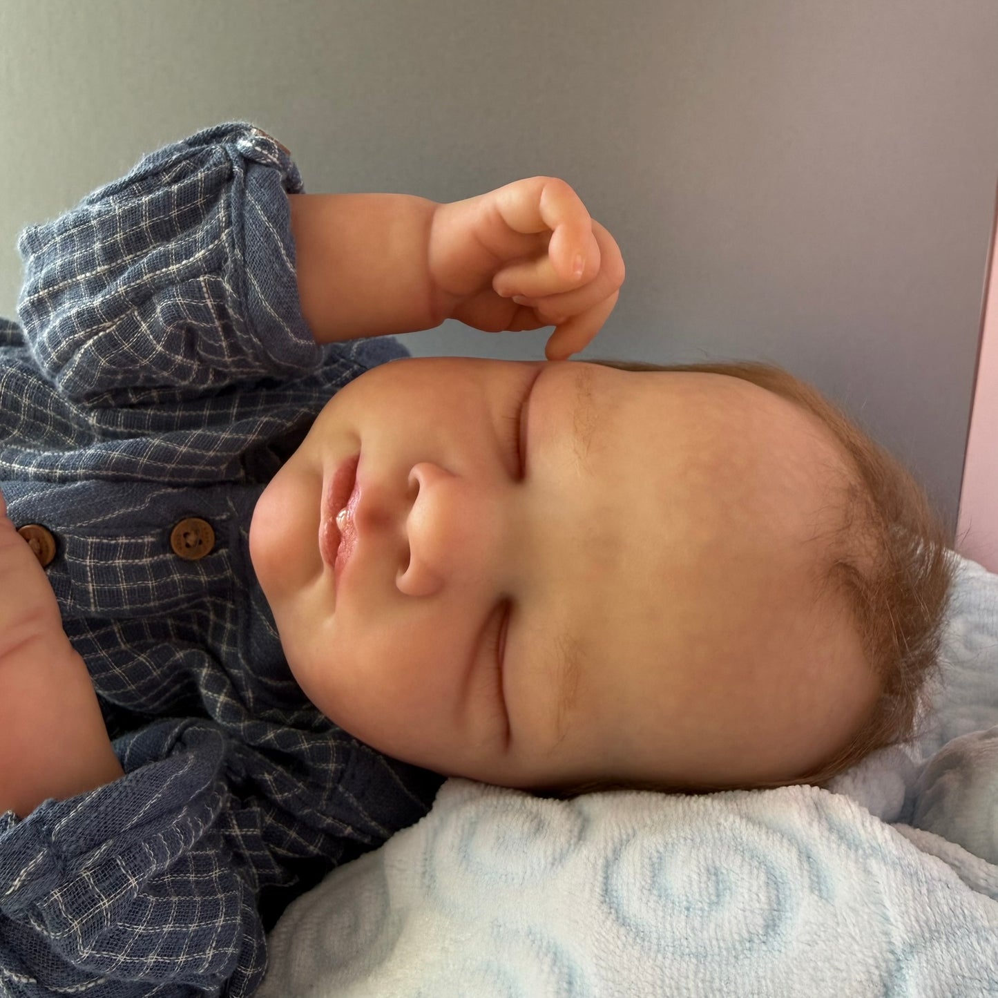Newborn baby wearing a blue checkered outfit on a light-colored blanket.